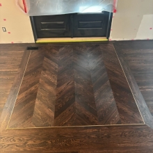 Red Oak flooring laid in a chevron pattern with a border and brass inlay.  An antique gold top step vent was also cut in to finish the look.  Floor was finished with Berger Seidle Base Oil in Ebony