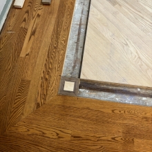 Carpet was removed from the center of the dining room. The space was then filled in on a 45 with a walnut / maple border and a walnut, oak and maple inlay. Oak was stained with Latte Macchiato with a satin finish on top.