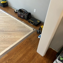 Carpet was removed from the center of the dining room. The space was then filled in on a 45 with a walnut / maple border and a walnut, oak and maple inlay. Oak was stained with Latte Macchiato with a satin finish on top.