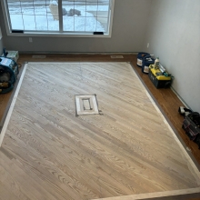 Carpet was removed from the center of the dining room. The space was then filled in on a 45 with a walnut / maple border and a walnut, oak and maple inlay. Oak was stained with Latte Macchiato with a satin finish on top.