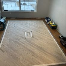 Carpet was removed from the center of the dining room. The space was then filled in on a 45 with a walnut / maple border and a walnut, oak and maple inlay. Oak was stained with Latte Macchiato with a satin finish on top.